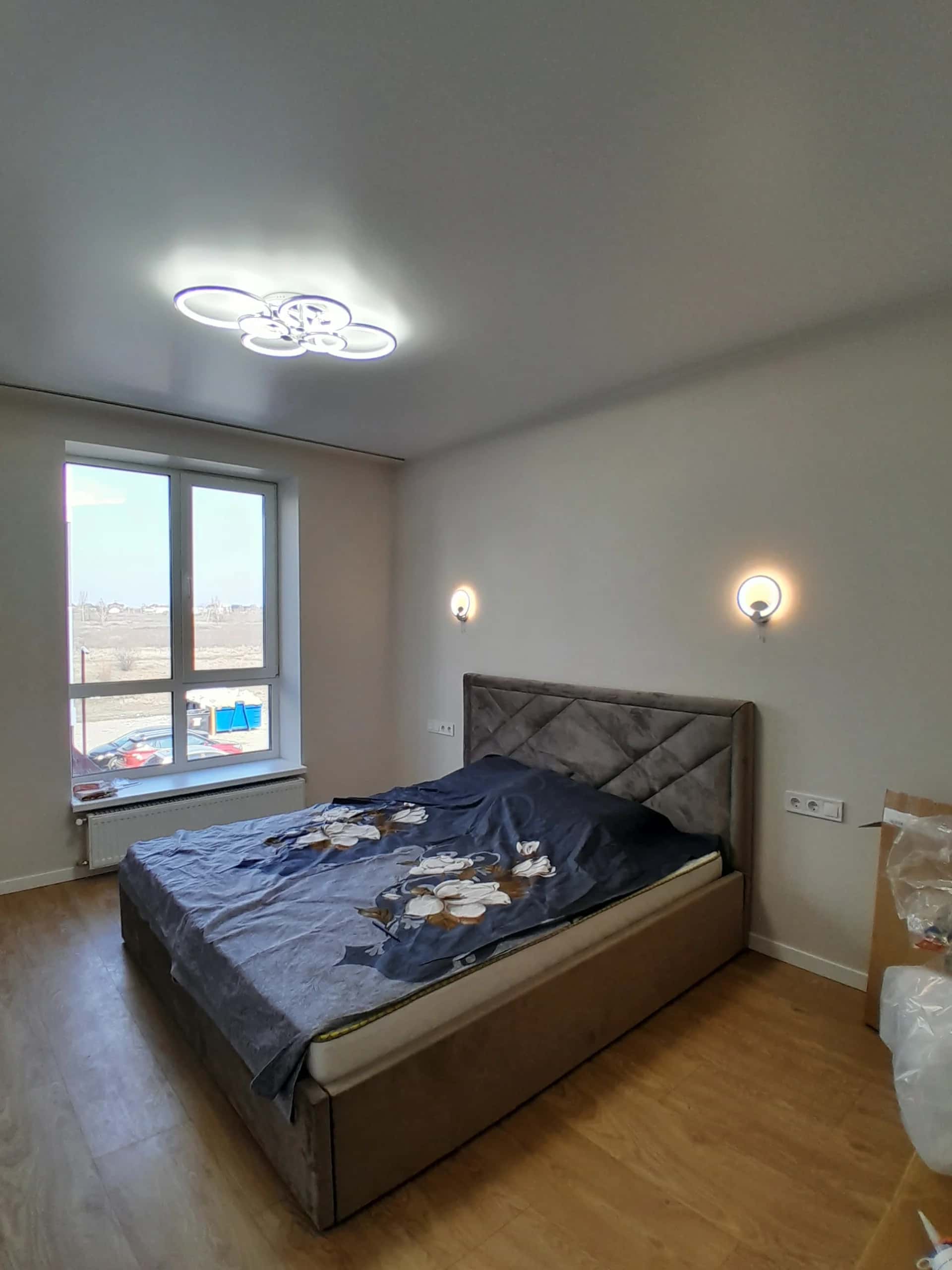 Bedroom with honey-toned laminate flooring, white walls, and two wall sconces beside the bed