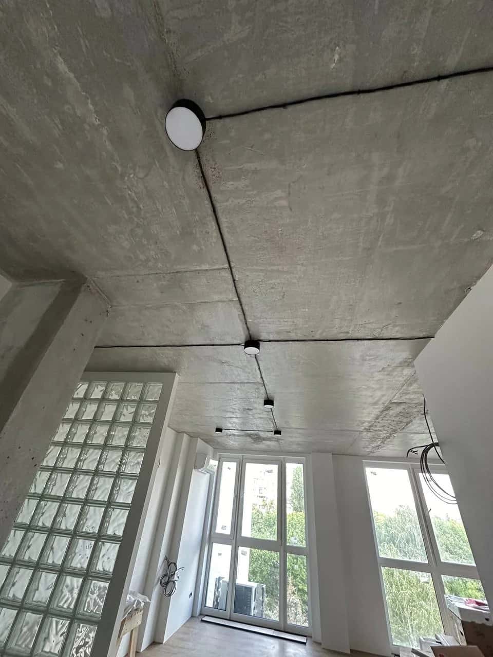 Living room: exposed concrete ceiling with open wiring and surface-mounted black-body light fixtures