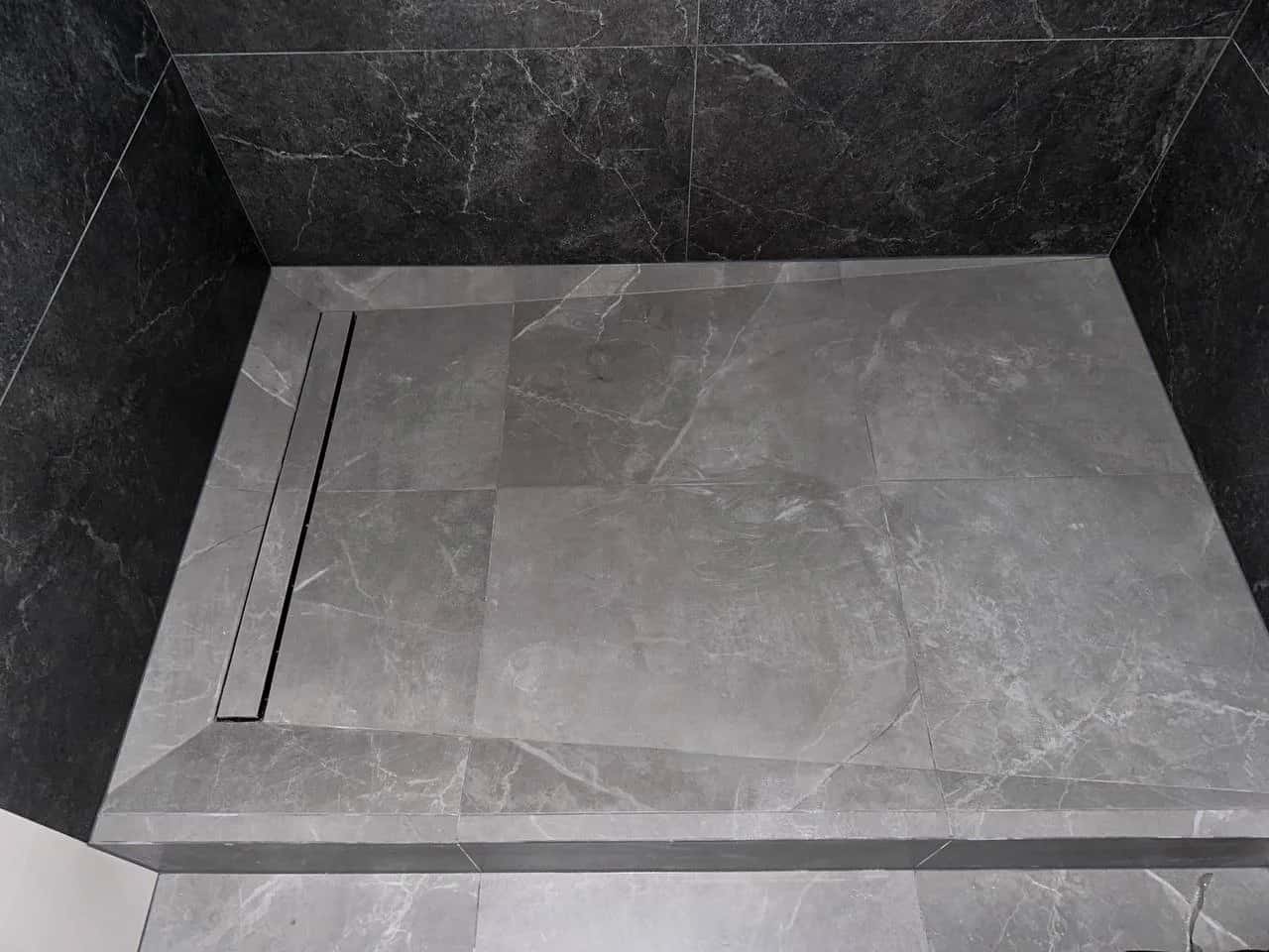 Shower enclosure clad in marble-look porcelain tile with a linear drain along the wall