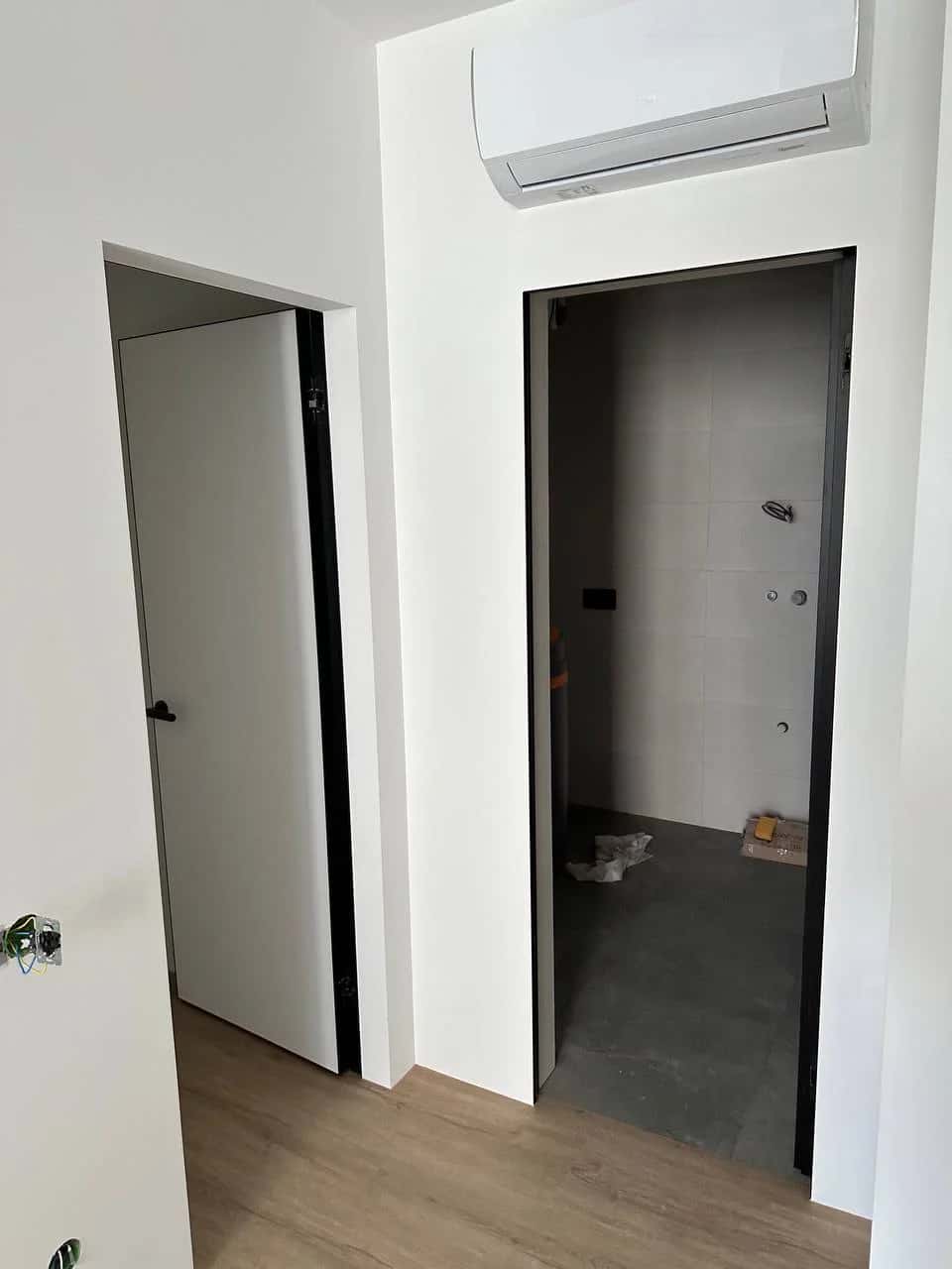Apartment corridor with two concealed doors featuring black edges and a split-system air conditioner on the wall