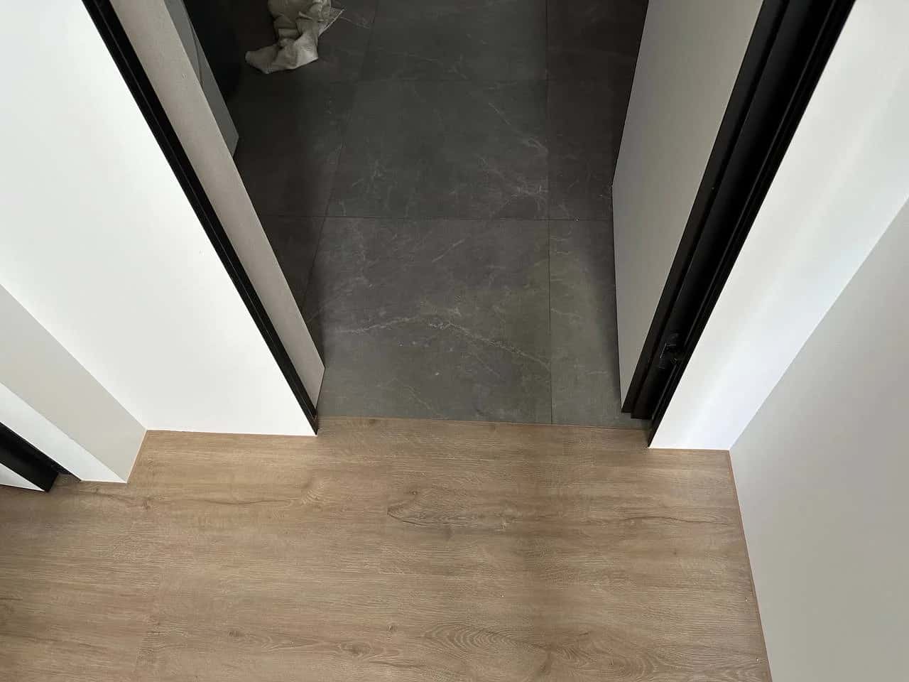 Floor junction at a doorway: vinyl plank meets dark marble-effect porcelain tile