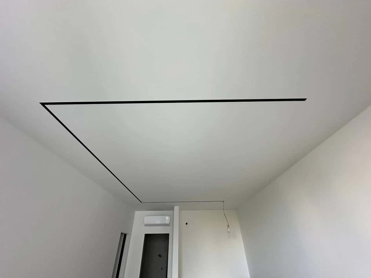 Room ceiling with a built-in linear light fixture in a black profile running along the perimeter