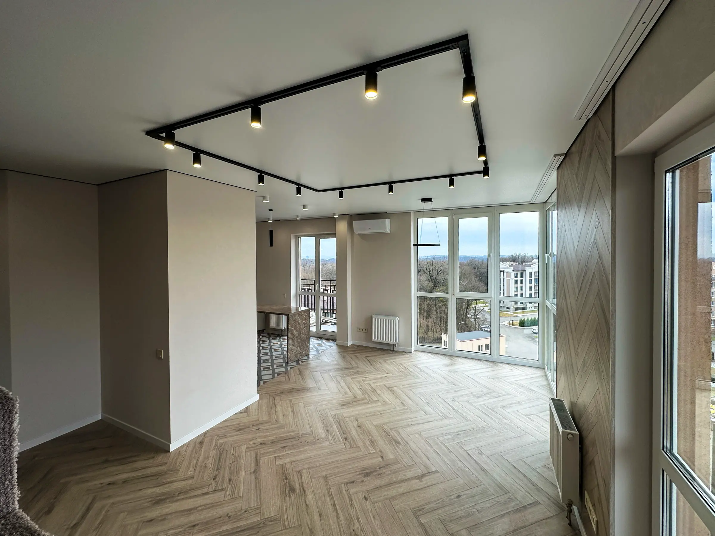 Living room with herringbone laminate flooring and track lighting on a white ceiling