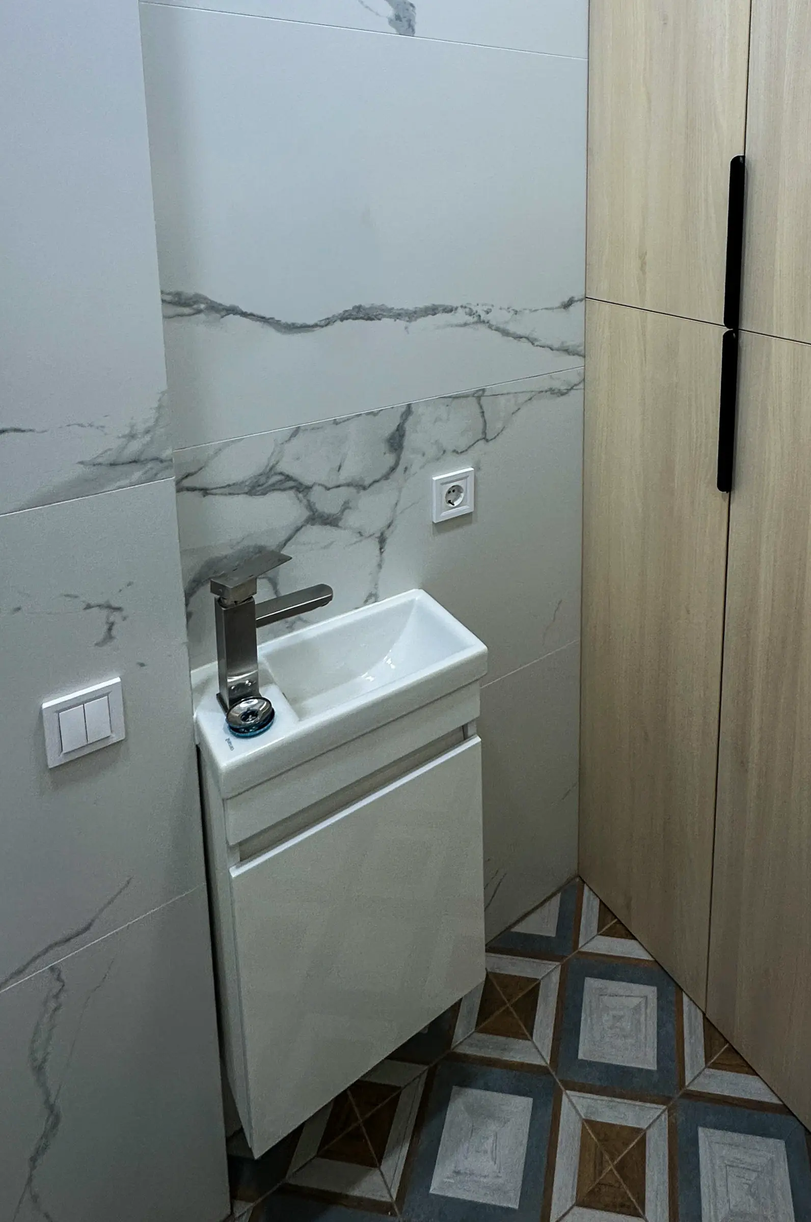 Bathroom: compact wall-mounted sink with a chrome faucet against marble-effect tiles