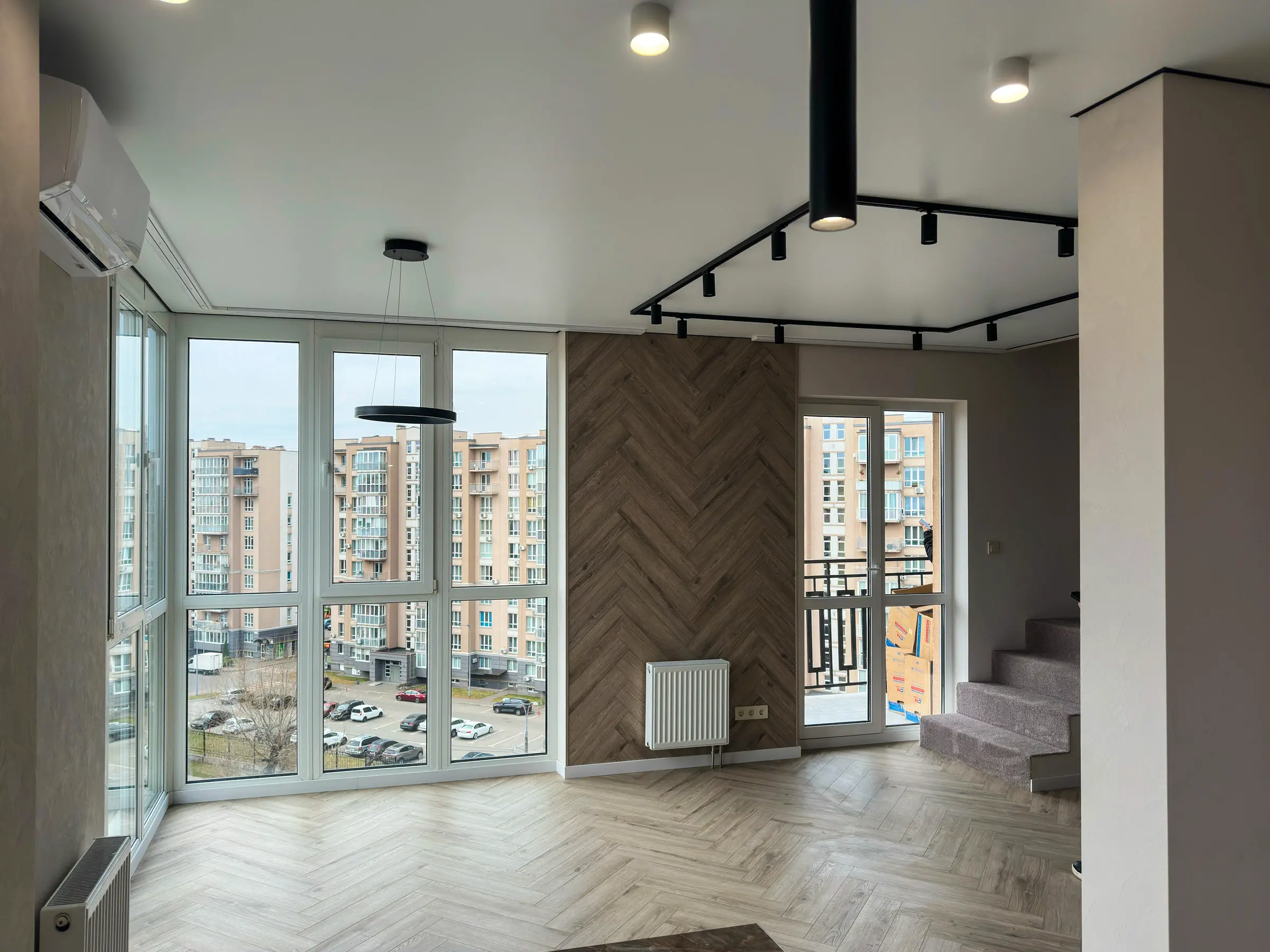 Living room with panoramic window: herringbone parquet floor and herringbone laminate accent wall