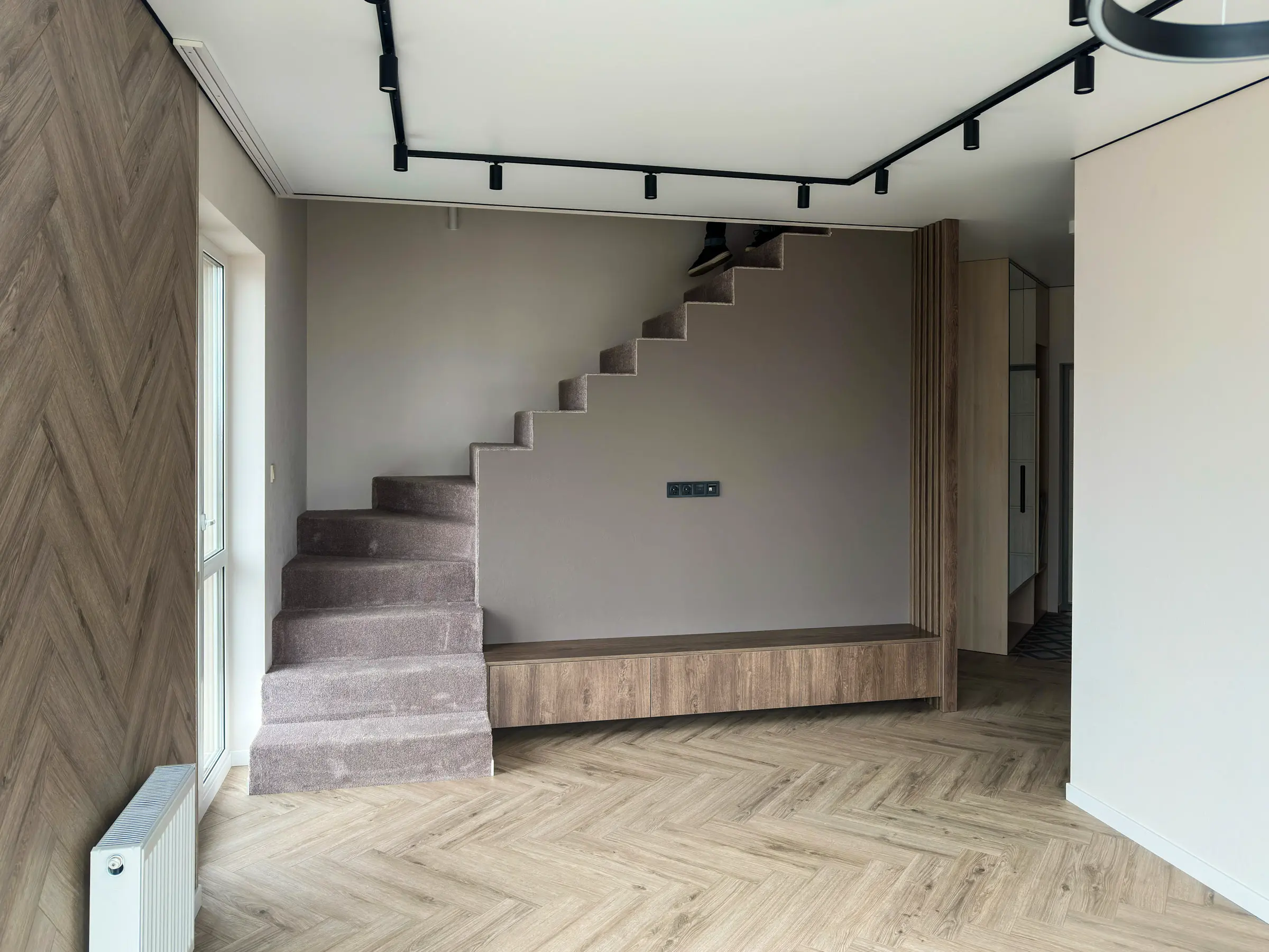 Living room with concrete stairs covered in carpet and a herringbone parquet floor