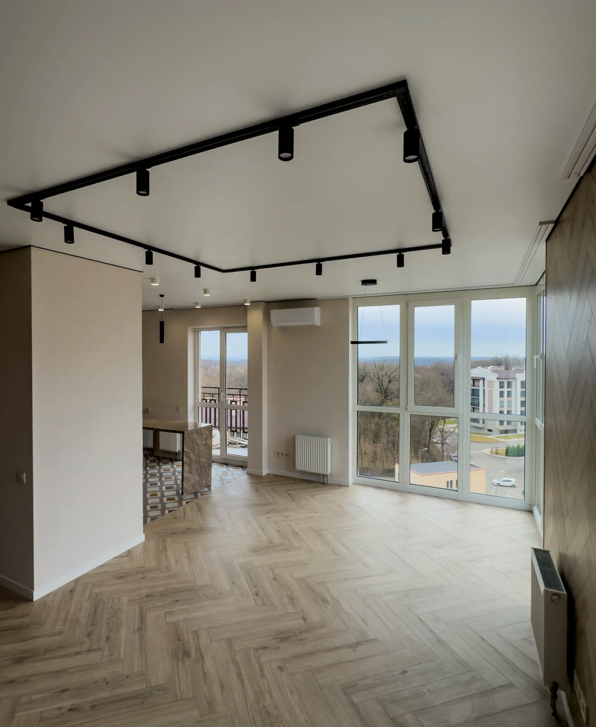 Living room with herringbone flooring and a black track lighting system on the ceiling