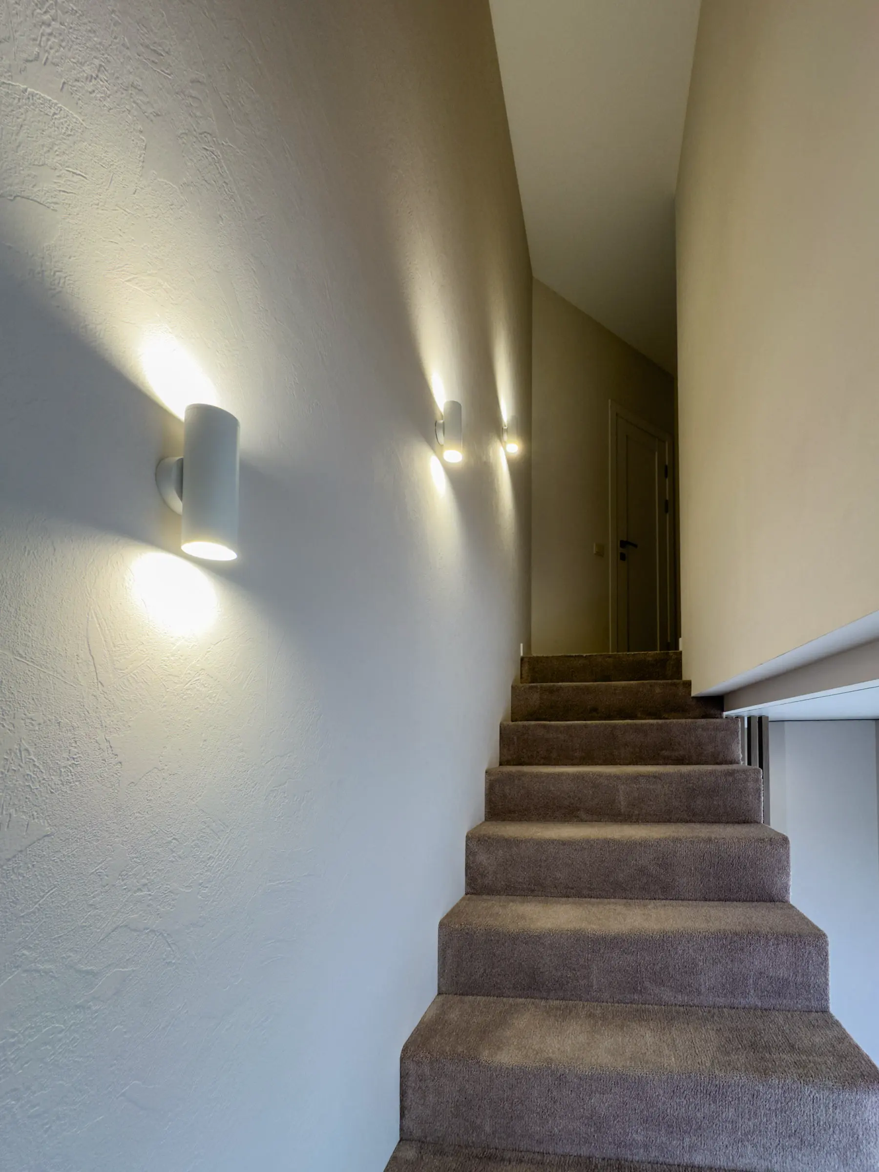 Stairwell with double-sided wall sconces and carpet-covered stairs