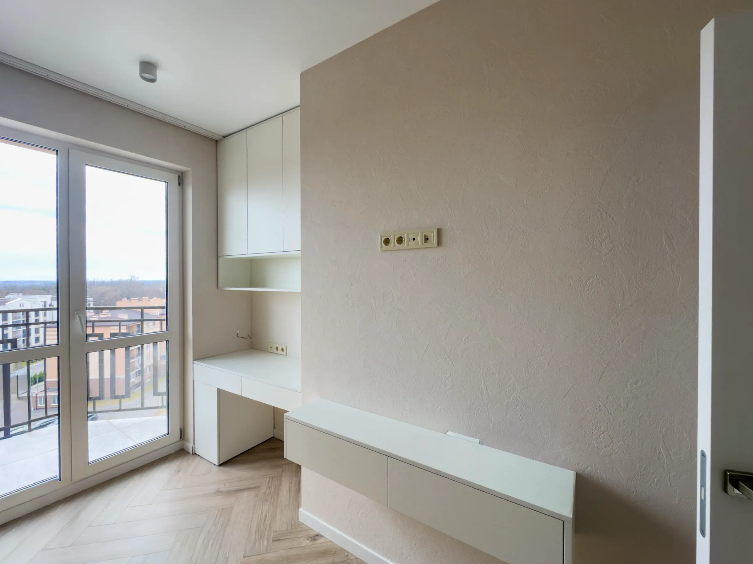 Room with built-in furniture: wall-mounted cabinet, open shelves and a desk by the balcony doors