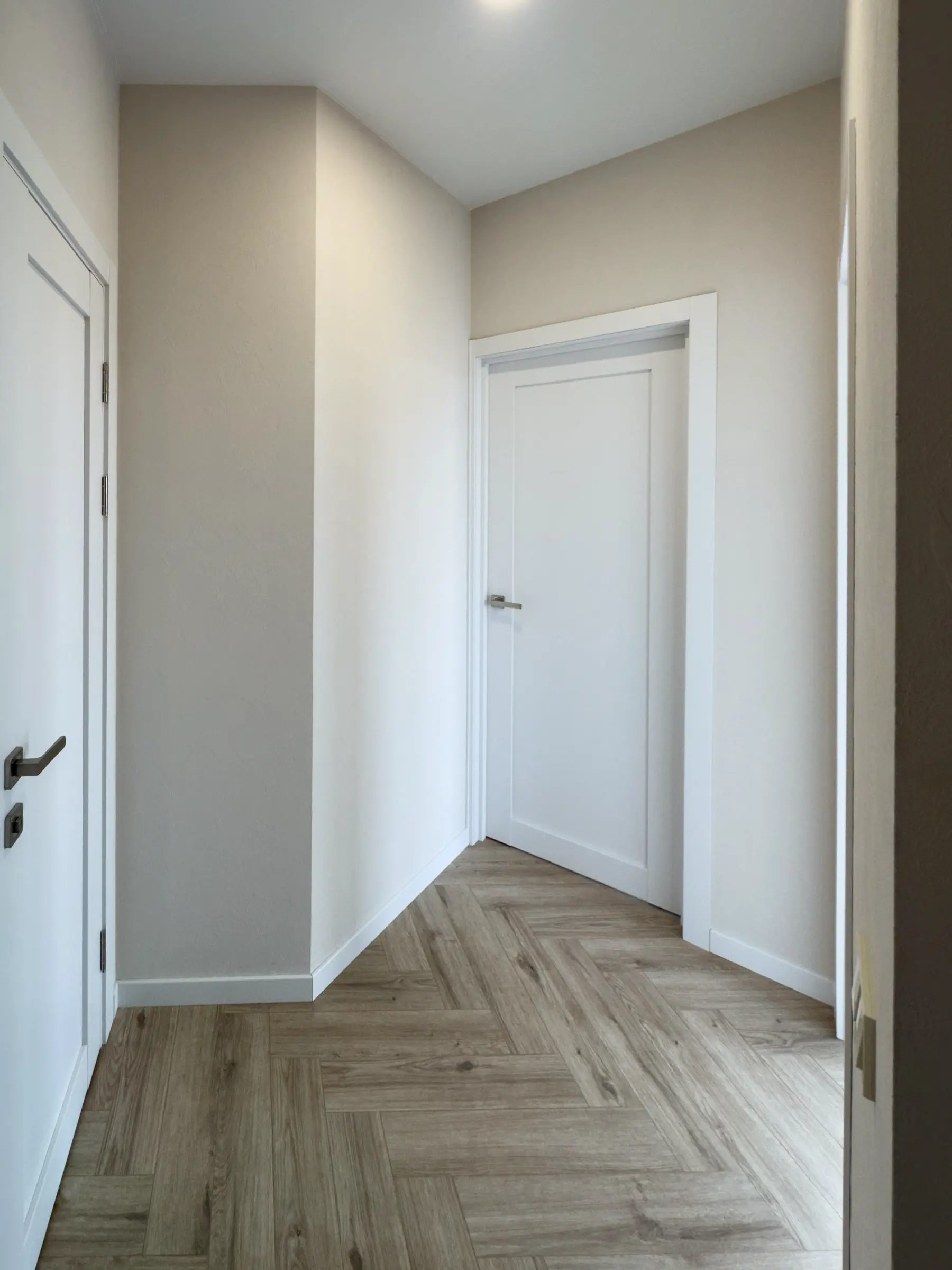 Apartment hallway with herringbone wood-effect porcelain tile flooring and white doors
